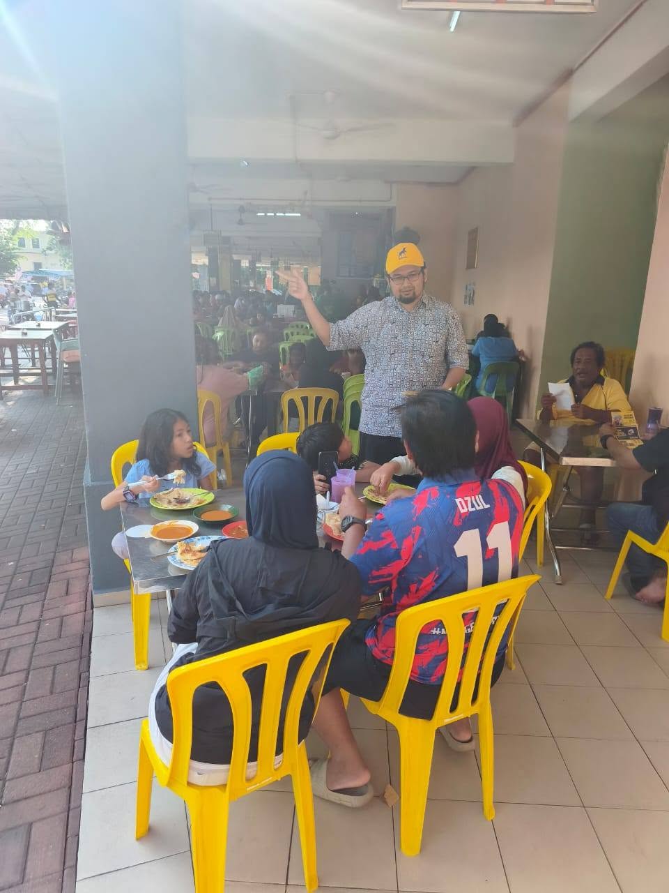 Aman Akil menyampaikan jemputan kepada pengunjung di sebuah kedai makan.